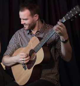 Harry Champion in profile, playing guitar and smiling.